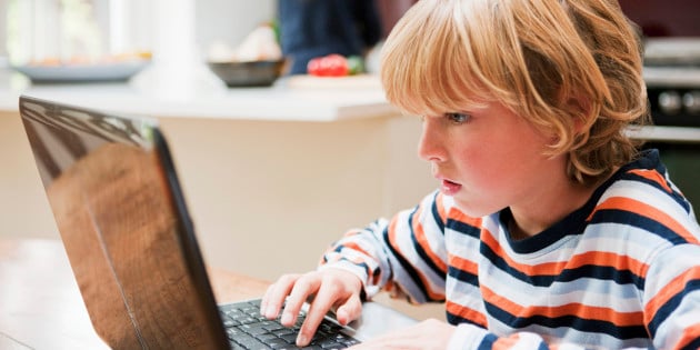 Young boy looking at a laptop monitor while typing
