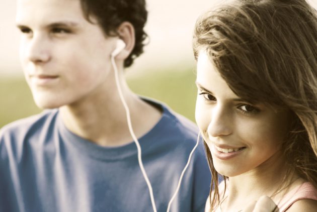 Teens sharing earphones, listening music outdoor.</span> <span class=