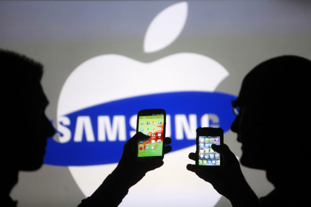 Men are silhouetted against a video screen as they pose with Samsung Galaxy S3 and iPhone 4 smartphones in this photo illustration taken in the central Bosnian town of Zenica, May 17, 2013.</span> <span class=